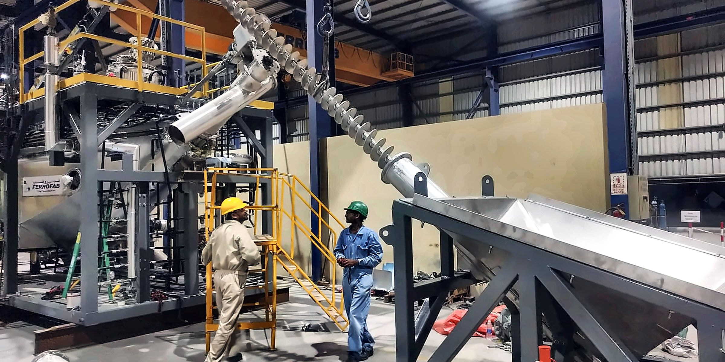 Industrial screw conveyor installation with workers beside the equipment
